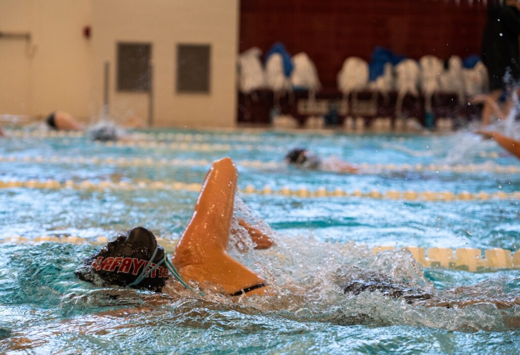 A swimmer glides through the laplane in the Lafayette pool with a Lafayette swim cap visible above the water.