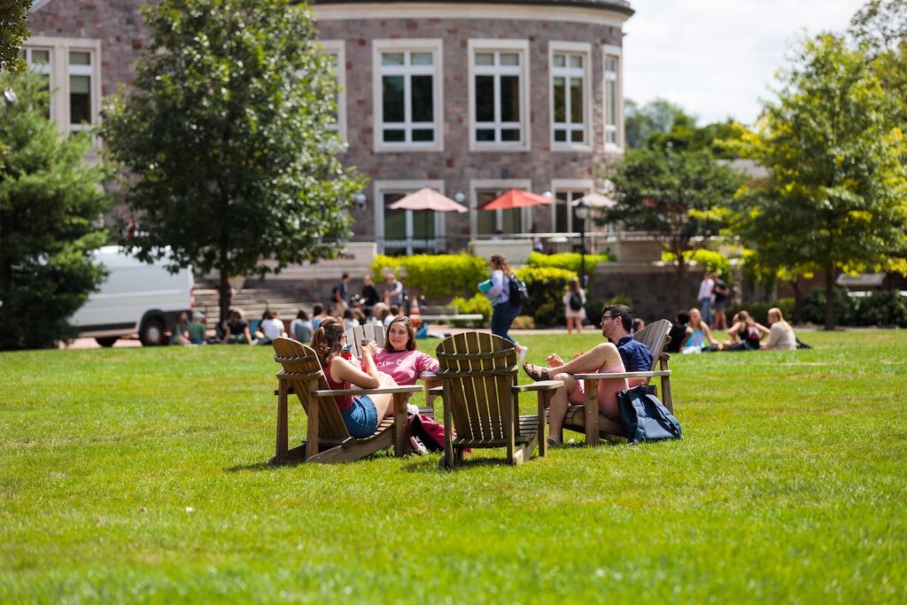 students sit in adirobdack chairs around the Quad