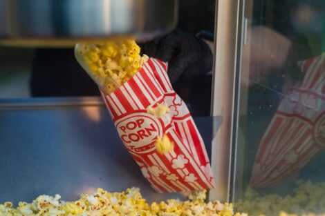 Popcorn is scooped into a red and white striped bag.