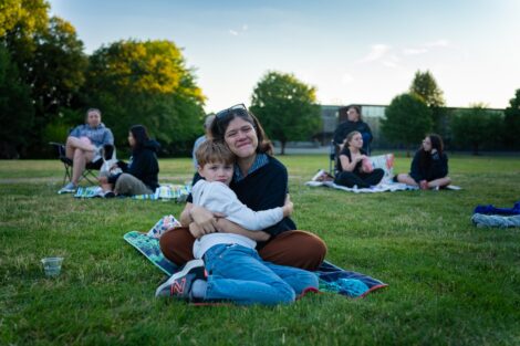 A staff member hugs a kiddo as they sit outside on the Quad watching a movie.