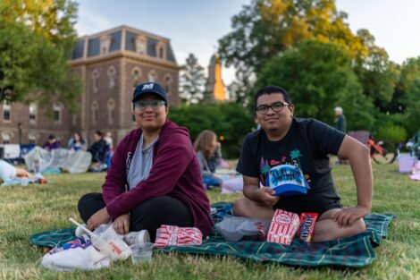 Two people sit on blankets with popcorn ahead of Movies on the Quad.