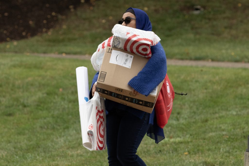 A student carries boxes across the grass during move in.