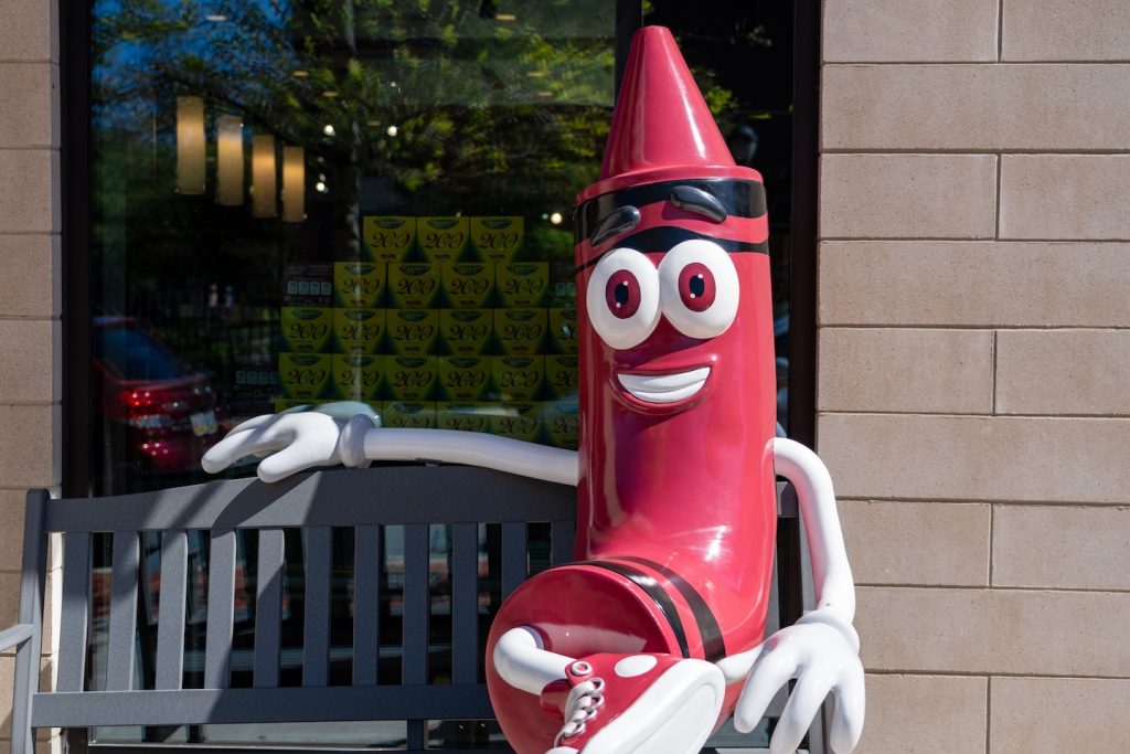 A maroon Crayola crayon sculpture sits on a bench by the College Store.